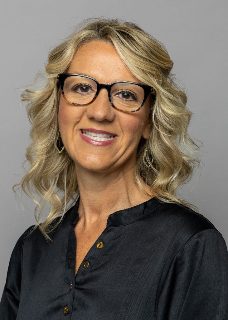 Andy Hayes, a smiling woman with wavy, should length blonde hair, wearing glasses and a dark shirt with buttons.